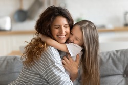 Affectionate beautiful young woman cuddling small preschool child daughter, feeling happiness. Cute little kid girl embracing loving mommy, feeling thankful, enjoying tender sweet time at home.