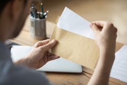 Close up businessman holding envelope with blank paper sheet, focused man looking at letter, received news, notification or invitation, working with correspondence, sitting at work desk