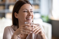 Smiling beautiful woman holding glass of pure mineral water close up, satisfied happy young female with perfect skin looking in distance, healthy lifestyle and natural beauty concept, dehydration