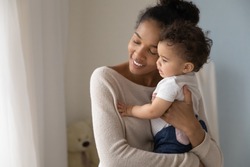 Loving african American mother hold in arms embrace little baby girl child enjoy tender family moment at home, caring young biracial mom hug cuddle cute toddler infant, childcare, maternity concept