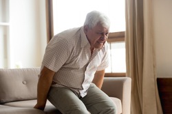 Sick mature 80s man stand from couch suffer from sudden lower back muscle spasm or strain, unhealthy senior 70s grandfather struggle with rheumatism, spinal ache or pain, elderly healthcare concept