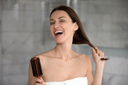 Head shot portrait 35s cheerful woman after take a bath holds hairbrush tidy her strong healthy hair, morning beauty routine lifestyle, treatment for perfect hair growth advertising, haircare concept
