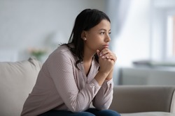 Concerned sad African woman sit on sofa in living room thinking of problem looks in distance feels depressed due loneliness, inner emptiness, life troubles, break up or divorce, marriage split concept
