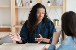 Close up confident african american businesswoman explaining new responsibilities to female applicant. Attractive young diverse woman hr manager talking and introduction company to job seeker.