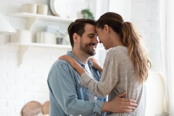 Happy millennial husband and wife hug cuddle enjoy tender romantic moment in kitchen, smiling loving young couple embrace on domestic date at home, having romance together, relationships concept