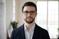 Head shot close up portrait of young confident businessman in eyeglasses. Smart professional bearded coach trainer speaker ceo executive in formal wear posing for photo alone, looking at camera.
