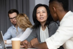 Focus to asian ethnicity middle-aged woman mentor more experienced worker teach African guy millennial intern, diverse staff members sitting in co-working shared room working on common project concept