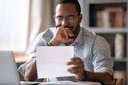 African man sit at desk hold postal correspondence letter read good news feel proud by personal business achievement, got hired, receive reward, financial success statement, approved bank loan concept
