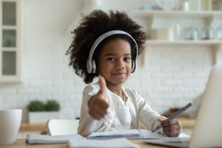 African girl in headphones enjoy e-learn sit at table showing thumbs up recommend e-study easy and interesting app for children, using modern tech. Homeschooling, clever kid and self-education concept
