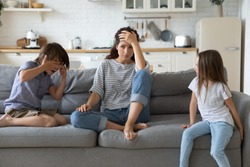 Hyperactive kids tired and complain near upset mother sitting at couch. Frustrating mom stressful feels headache at home. Fatigue parent doesn't want to play with son and daughter.