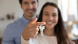 Close up young excited couple showing keys in hands to camera. Happy homeowners celebrating moving in new apartment or last banking mortgage payment, feeling glad of purchasing property, real estate.