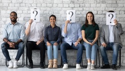 Smiling diverse candidates applicants sitting in row with unknown people holding paper sheets with question marks, successful hired man and women getting job, employment and recruitment concept