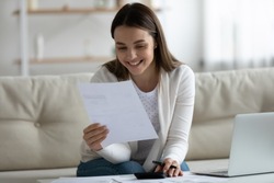 Smiling young beautiful woman reading banking paper notification about last mortgage payment while calculating budget at home. Happy millennial girl feeling excited of good news in letter notice.