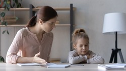 Strict mother scolding upset little daughter for bad marks, sitting at table at home, angry serious mum lecturing lazy unmotivated schoolgirl, children education problem, parent and child conflict