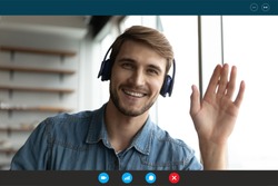Screen view portrait of smiling young Caucasian man in headphones wave greet talk speak on video call at home. Happy male in earphones have webcam virtual digital conference on computer online.