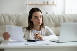 Serious young woman look at laptop screen busy managing household finances expenditures paying bills online. Pensive millennial female take care of budget count expenses, make payment on computer.