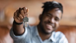 Close up blurred background view of excited African American male renter show new house keys buy first home. Happy biracial man tenant excited with moving relocation. Real estate, realty concept.