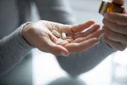 Pharmacy and healthcare. Close up of young female hands holding opened pill bottle and two soft-shelled capsules taking medicine for flu, influenza, painkiller, vitamin complex, oral contraceptives