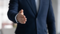 Close up crop image young businessman reaching out hand for shaking, proposing good deal to partner, making greeting gesture to client, welcoming new employee at work, congratulating with achievement.