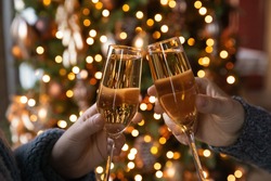 Crop close up of man and woman hold glasses with champagne clink greet congratulate with New Year. Couple celebrate Christmas winter holidays at home together, wish luck and joy. Celebration concept.