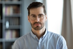 Head shot young attractive businessman in glasses standing in modern office pose for camera. Videoconference call profile picture handsome entrepreneur portrait, professional occupation person concept