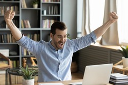 Happy businessman looks at laptop screen read great e-mail news raised arms up celebrates career advance seated at desk. Success at business, online auction win. Opportunity, moment of victory concept