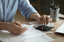 Personal finance management, accounting concept. Close up view man sitting at table using calculator performs arithmetic operations calculates costs per month, manage family budget, control expenses