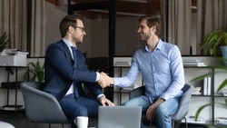 Two happy male business partners handshaking reaching agreement on negotiations, smiling leader greeting skilled capable worker employee with reward promotion, content client and banker finishing deal