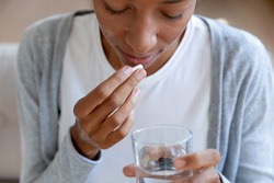 Crop close up of young African American woman feel unhealthy drink medicine with water. Unwell biracial female have pill or drug, take daily dose of vitamins or supplements. Healthcare concept.