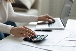 Close up young woman using calculator and laptop, checking domestic bills, sitting at table with financial documents, managing planning budget, accounting expenses, browsing internet service