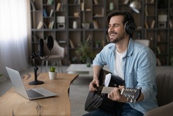 Wide banner view of happy millennial male artist hold guitar take online video webcam lesson on computer. Smiling young man singer or composer use instrument watch music tutorial on laptop at home.