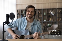 Portrait of smiling millennial Caucasian male singer or composer hold guitar record new single at home studio. Happy young 20s man artist compose song play on electric music instrument. Hobby concept.