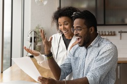 Happy young African American couple feel euphoric read good unbelievable news in paper letter correspondence. Overjoyed biracial man and woman triumph get pleasant message in paperwork.