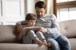 Caring young Caucasian father relax on couch with little son learn reading books on weekend together. Loving dad and small 6s boy child study at home, prepare for school. Children education concept.