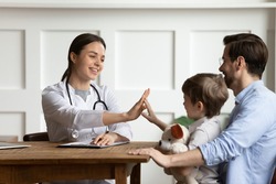 Caring female doctor give high five with small boy patient visit hospital with father. Smiling woman pediatrician greet with happy little child at consultation in clinic with dad. Healthcare concept.
