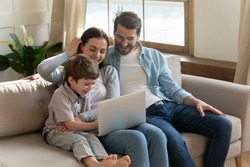 Smiling parents relax on sofa in living room with small 7s son child have fun browsing using modern laptop together. Happy young Caucasian family with little boy kid watch funny video on computer.