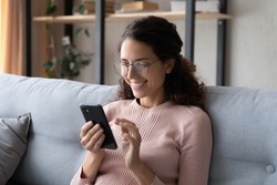 Happy millennial woman relaxing on comfortable sofa, enjoying web surfing information in internet or using mobile software application, communicating distantly with friends in social networks at home.