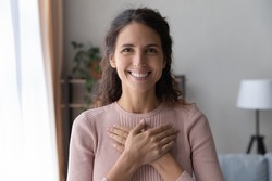 Portrait of happy millennial female volunteer holding folded hands on chest, looking at camera. Kind smiling young woman feeling thankful, showing appreciation, gratitude believe charity concept.