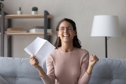 Emotional joyful millennial woman in glasses holding paper sheet in hands, getting dream job offer or university admission letter, celebrating professional success, reading loan approval notification.