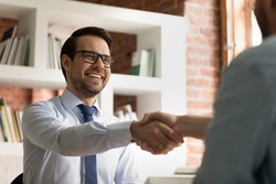 Smiling young Caucasian businessman shake hand of partner or colleague close deal after successful meeting in office. Happy male CEO or employee handshake get acquainted greet with business client.