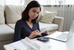 Concentrated millennial vietnamese female engaged in home banking using calculator and laptop. Attentive asian woman count taxes rental tenancy sum to pay online control accounts review utility bills