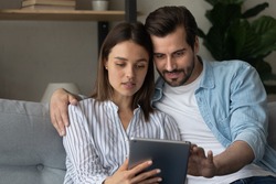 Focused married couple read insurance policy loan contract text from bank website on tablet screen planning to make treaty. Serious young spouses hold digital pad device buy goods order service online