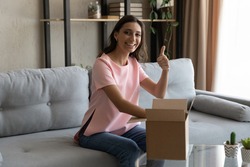 Young arab female loyal client of delivery service web shop open package show thumb up positive feedback. Portrait of indian lady blogger unpack box with ordered product look at camera recommend goods