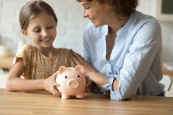 Good choice. Cropped shot of happy mom embracing little daughter with funny piggybank praise child for making wise decision to save pocket cash. Small kid girl plan to collect money for future needs