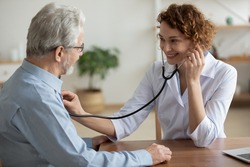 Smiling young Caucasian female doctor hold stethoscope listen to elderly male patient heart rate. Happy caring woman nurse use phonendoscope measure heartbeat of mature man in hospital.