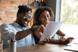 Excited young black husband wife read paper loan mortgage contract life insurance policy satisfied with good conditions offered. Smiling african couple receive tax refund letter glad to get money back