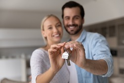 Close up focus of happy young Caucasian couple show keys to first share own apartment or house. Smiling millennial man and woman celebrate relocation to new home. Moving, rental, estate concept.