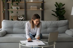 Smiling woman using laptop, managing finances, planning budget, sitting on couch at home, checking financial documents, domestic bills, browsing online banking service, satisfied by money refund