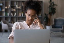 Pensive young biracial woman in glasses look at laptop screen work online think of problem solution. Thoughtful millennial African American female unmotivated to do computer job. Laziness concept.