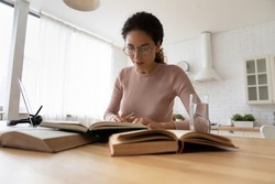 Engaged in paperwork. Serious young latina woman post graduate student sit at desk focused on preparing diploma paper work on degree. Young female scientist in glasses read books carrying out research